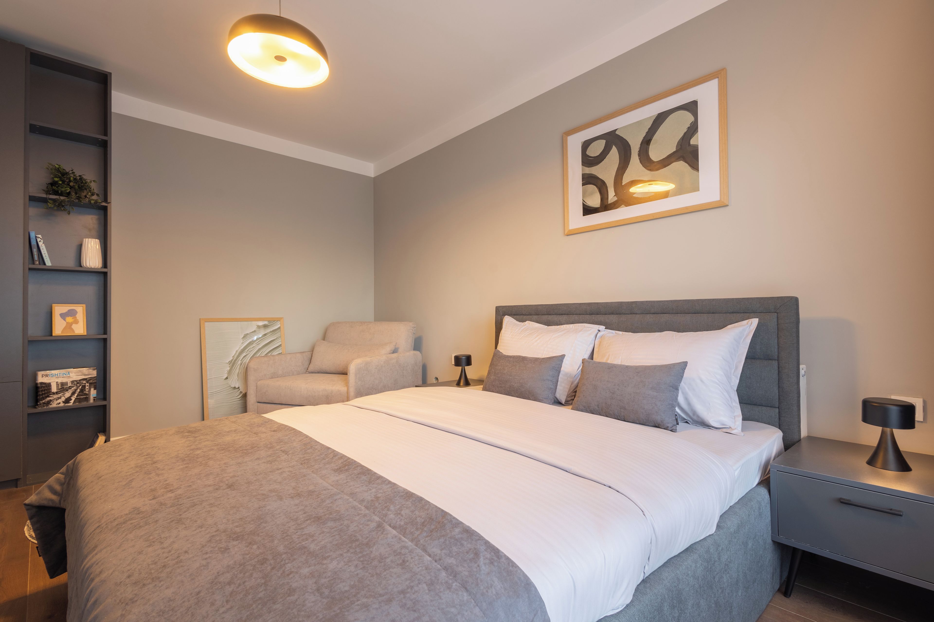 Un dormitorio moderno con una cama grande, una mesita de noche, una silla y una estantería.