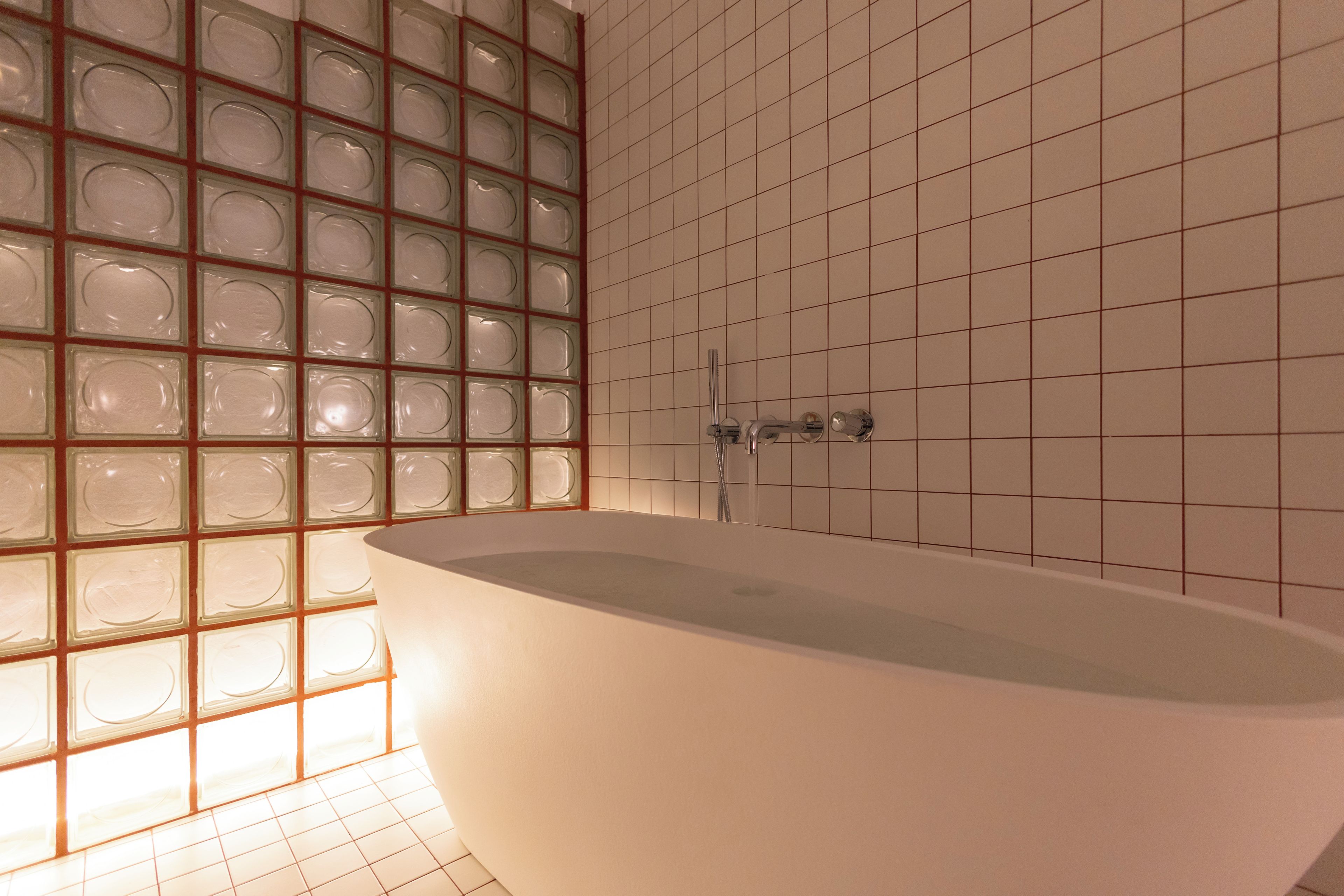 A modern bathroom with a freestanding bathtub, tiled walls, and a glass block wall.