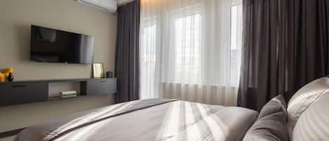 Une chambre d’hôtel moderne équipée d’un lit, d’un téléviseur à écran plat, d’une table de chevet et d’une fenêtre avec des rideaux.