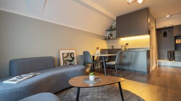 Ein modernes Wohnzimmer mit einem grauen Sofa, einem Couchtisch und einem Essbereich mit Stühlen. Im Hintergrund ist eine Küche zu sehen.