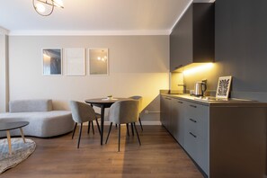 A modern kitchen with a dining area, featuring a round table, two chairs, and a sofa. - Prishtina City Apartments (Pristina)
