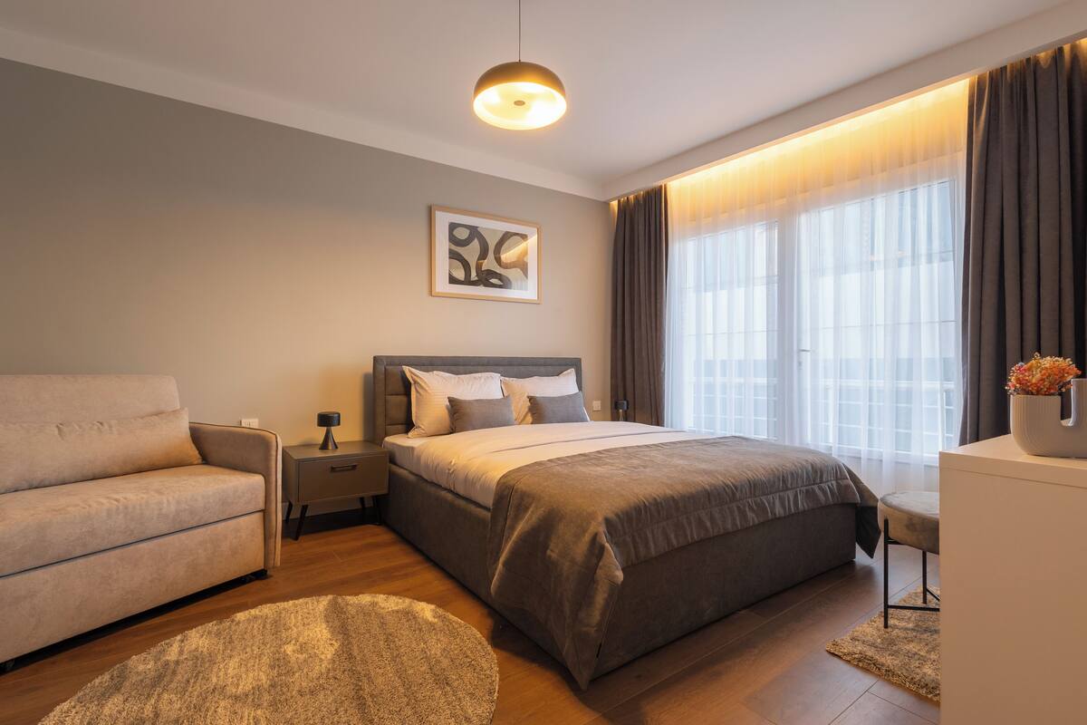 A modern bedroom with a bed, a sofa, a nightstand, and a desk.
