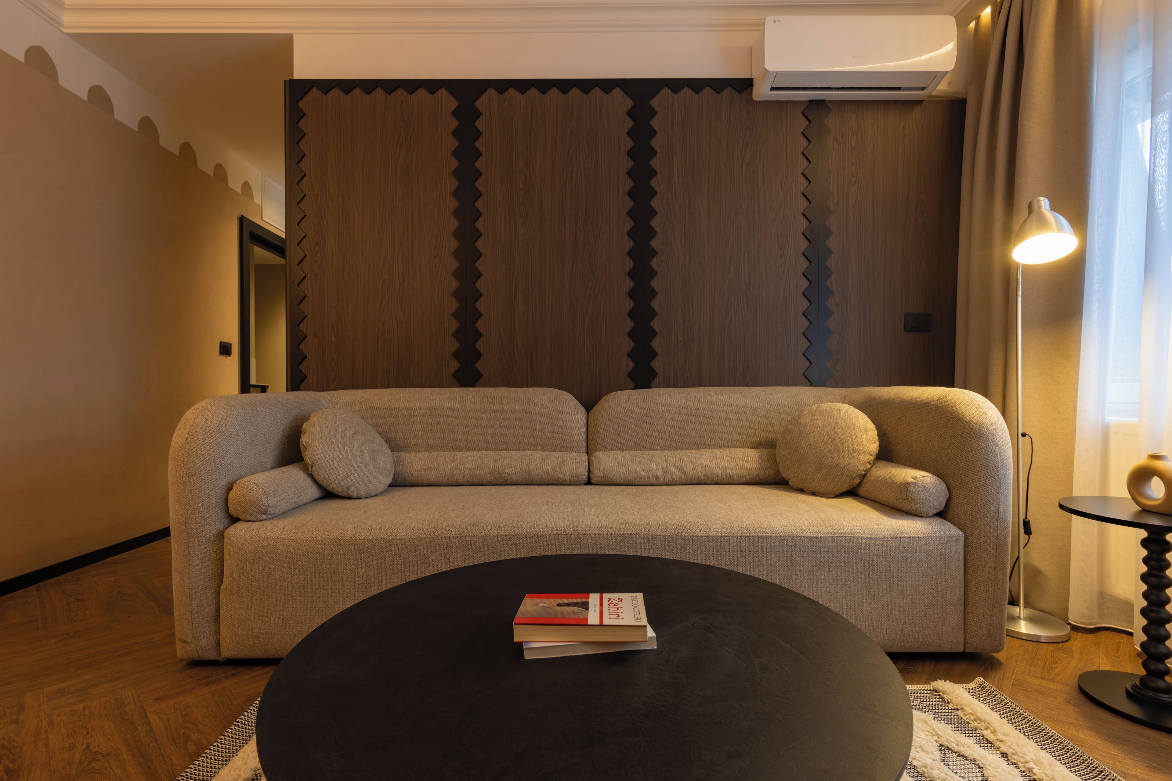 Un salon moderne avec un canapé, une table basse sur laquelle repose un livre, une lampe et un tapis à motifs.