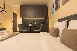 Habitación de hotel con cama, escritorio, sillas, kitchenette y obras de arte en las paredes.