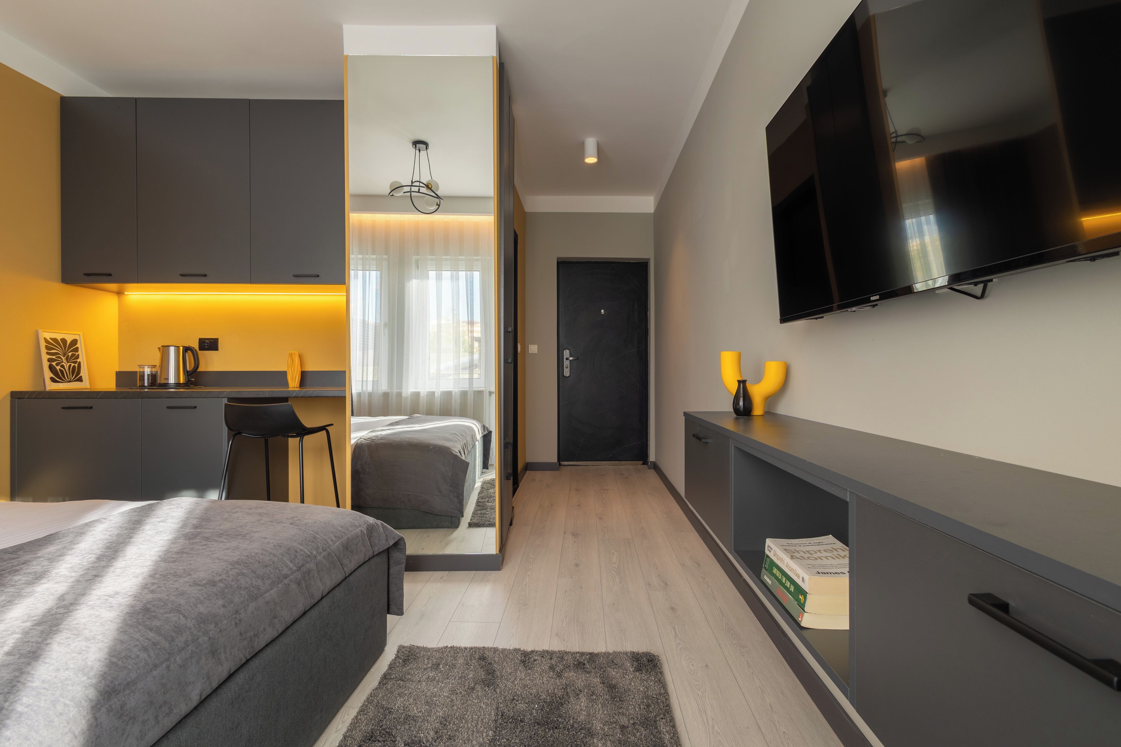 Ein modernes Hotelzimmer mit Bett, Schreibtisch, Fernseher und Küchenzeile.