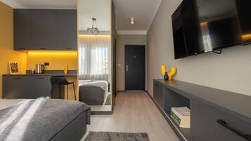 Ein modernes Hotelzimmer mit Bett, Schreibtisch, Fernseher und Küchenzeile.