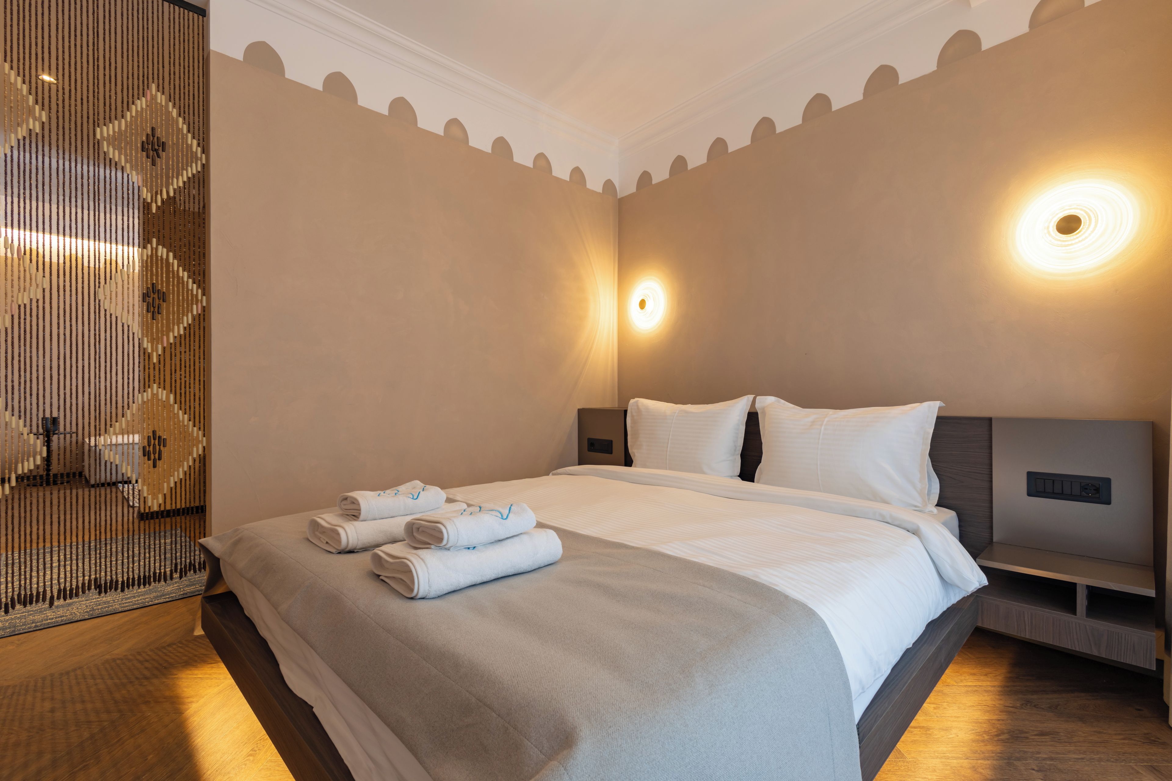 Una habitación de hotel con una cama grande, dos mesitas de noche, una lámpara de pared y un panel decorativo.