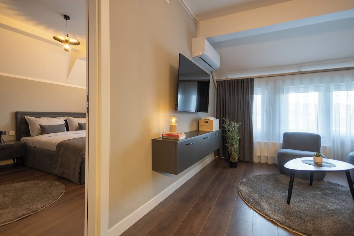 A modern hotel room with a bed, bedside table, TV, and a seating area with a table and chair.