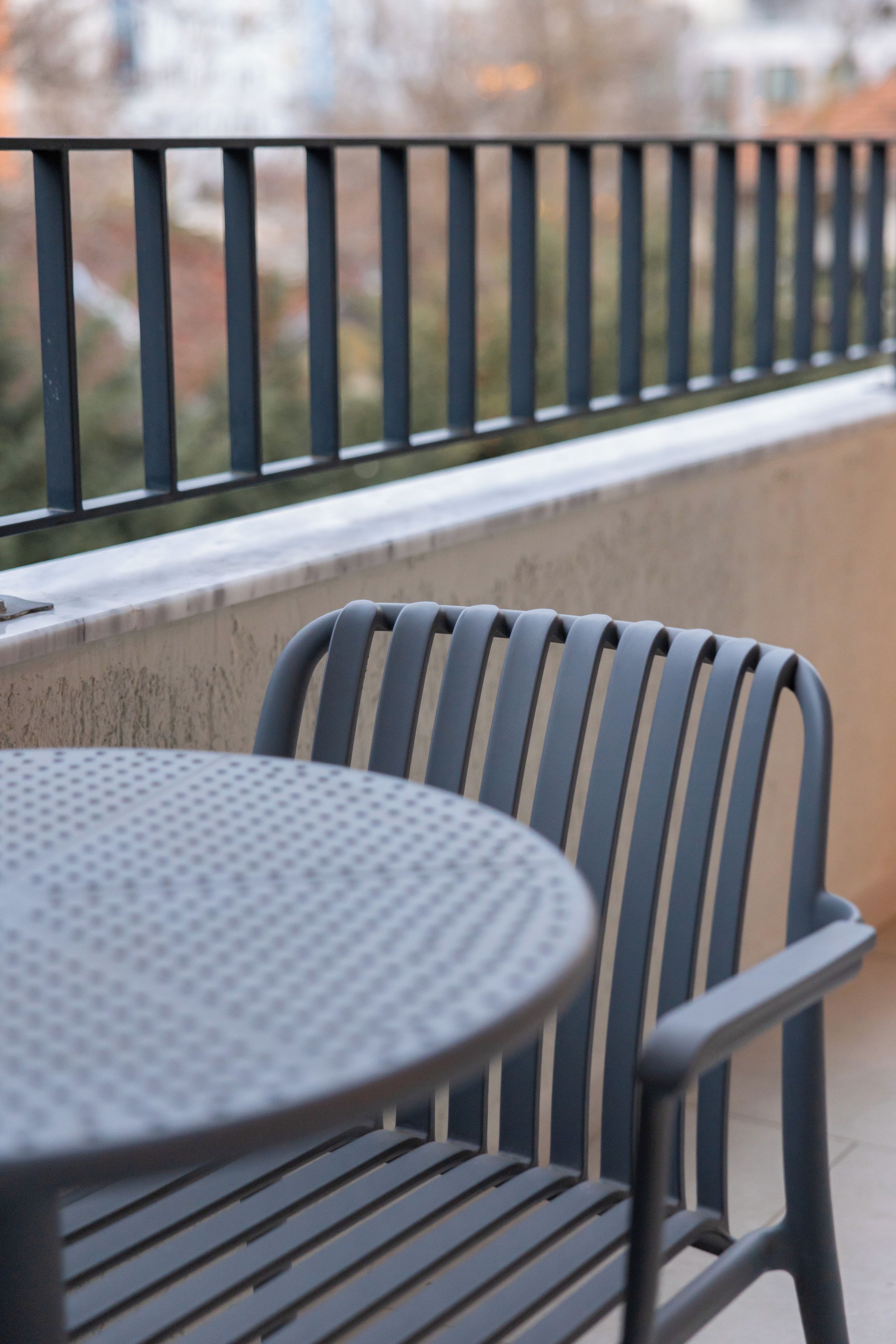 Een balkon met een metalen hekwerk, een ronde tafel en een stoel.
