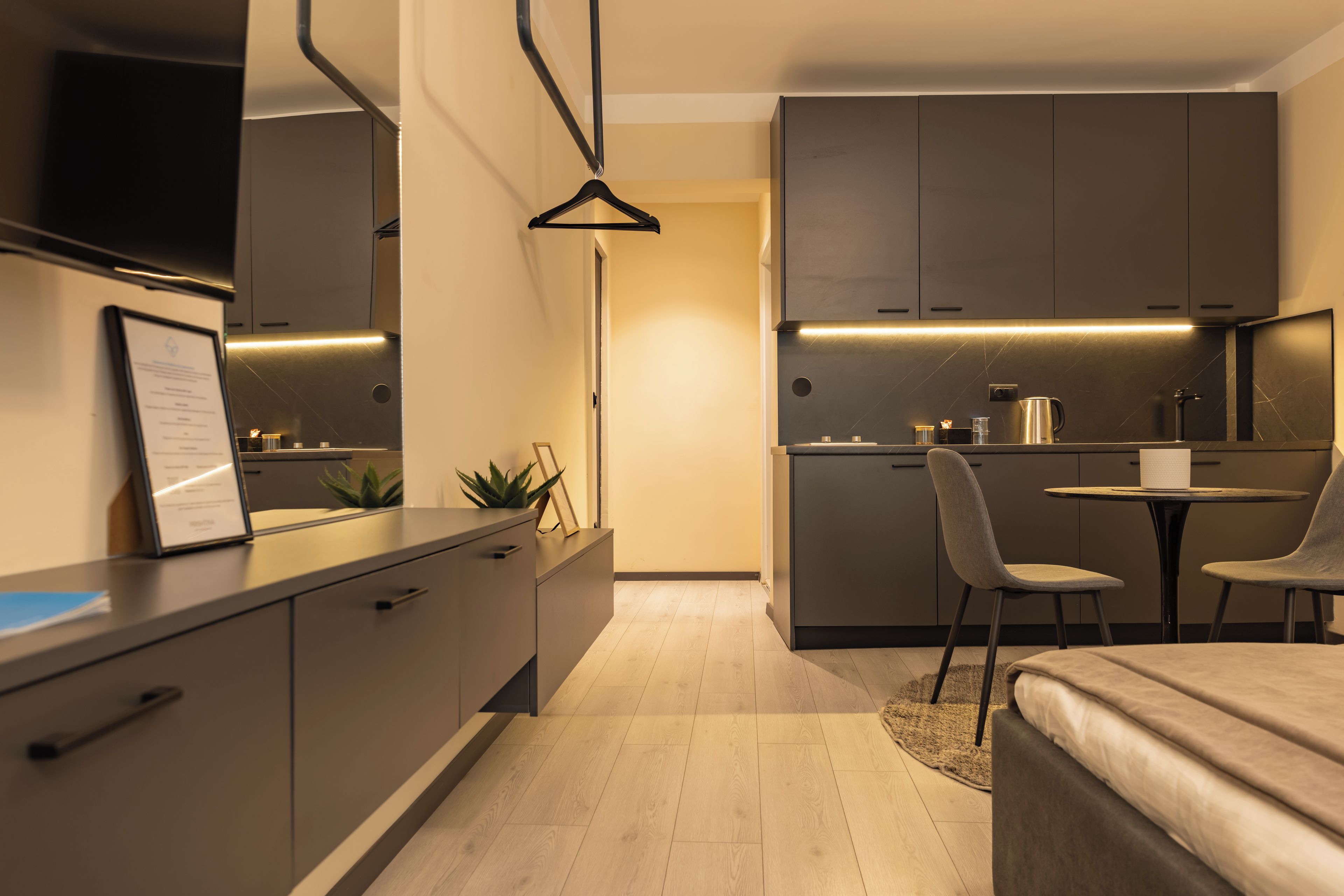 A modern hotel room with a kitchenette, a dining area, and a bed.