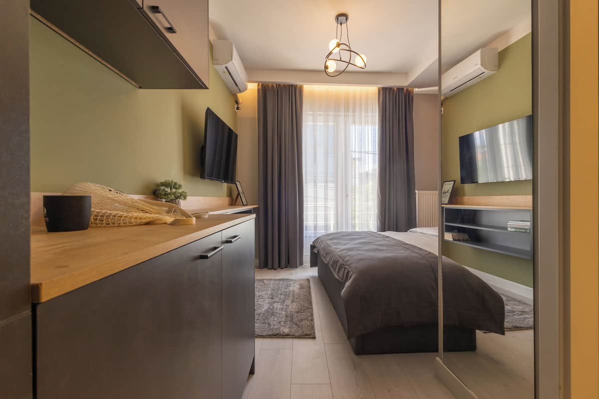 A modern bedroom with a bed, bedside table, TV, and a large window with curtains.