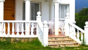A white building with a covered porch, a wooden door, and a staircase leading to a balcony with white railings. - SAONA VILLAS (VN ELEN): villa for 6 people, private pool, wifi, air conditioning (Les Tres Cales)