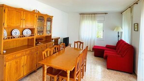 A dining area with a wooden table and chairs, a red sofa, and a TV on a wooden cabinet. - SAONA VILLAS (VN ELEN): villa for 6 people, private pool, wifi, air conditioning (Les Tres Cales)