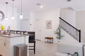 A modern kitchen with a central island, a dining area with a sofa and chairs, a staircase with a railing, and a door labeled 'OWNERS CLOSET'. - Entire Beautiful 5-bedroom Rental Minutes From Disney!  -No Pets Allowed- (Davenport)