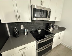 Uma cozinha moderna com eletrodomésticos de aço inoxidável, backsplash em azulejo preto e armários brancos.