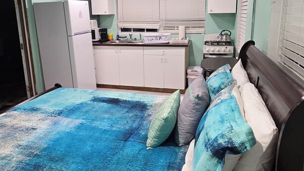 A bedroom with a bed, a nightstand, a dresser, a window with blinds, and a kitchenette with a refrigerator, stove, and microwave. - Centrally located 1 bedroom efficiency (georgetown)