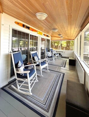 A covered porch with rocking chairs, a wooden ceiling, and a view of the outdoors.