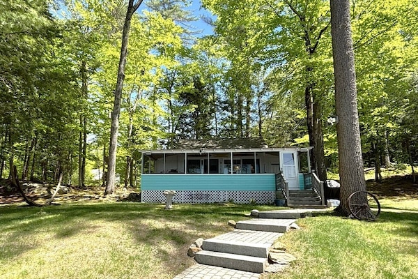 A charming turquoise cottage nestled in a lush, tranquil forest, offering a peaceful woodland retreat just steps away from Webster Lake.