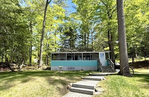 A small cabin with a porch, surrounded by trees.
