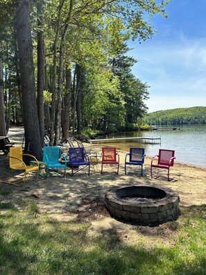 A lakeside campsite with a fire pit and colorful chairs.