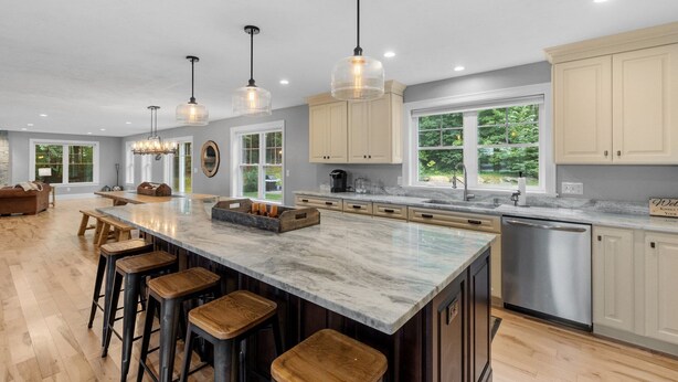 A spacious kitchen with a large island, wooden stools, pendant lighting, and a view of greenery outside. - Sunset Retreat at Dockham Shore (Gilford)