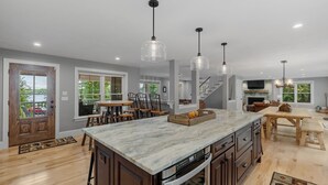 A modern kitchen with a marble island, stainless steel appliances, and pendant lighting. - Sunset Retreat at Dockham Shore (Gilford)