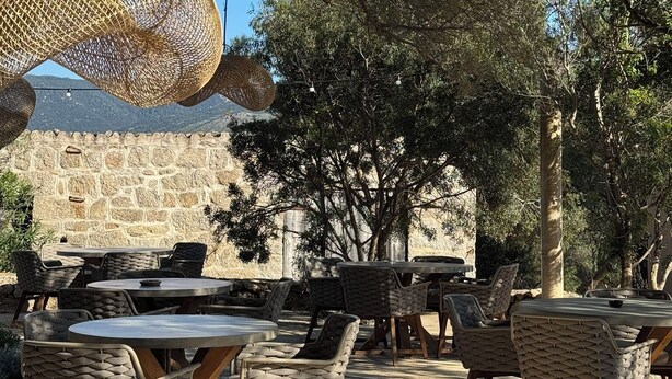 An outdoor seating area with wicker furniture and hanging rattan lamps, set against a backdrop of trees and a stone wall. - Hôtel confidentiel Le Grécale **** (Pianotolli-Caldarello)