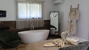 A modern hotel room with a large bed, a green chair, a bathtub, a mirror, and a robe rack. - Hôtel confidentiel Le Grécale **** (Pianotolli-Caldarello)