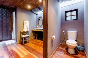 A compact bathroom with a wooden floor, a white toilet, a small sink, and a window. - Rainforest Paradise (Rio de Janeiro)