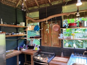 A rustic kitchen with wooden shelves, a gas stove, and hanging pots.
