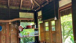 Una cocina rústica con techo de paja, estantes de madera y un amplio ventanal con vistas a la vegetación.