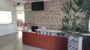 A hotel reception desk with a tiled wall, a plant, and a sign indicating a café operating from 6:30 to 9:00 hours. - Hotel Viracopos de Indaiatuba Ltda EPP (Indaiatuba)