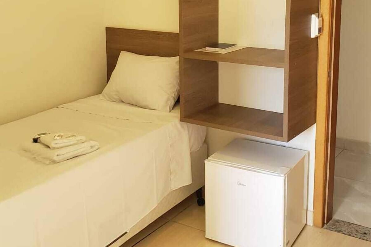 Une petite chambre à coucher, bien rangée, avec un lit simple, une armoire et un petit appareil électroménager blanc.