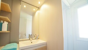 A bathroom with a white sink, wooden cabinets, a mirror, and a window.