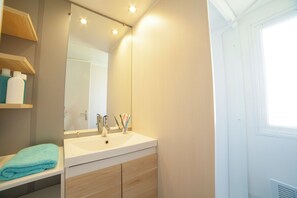 A bathroom with a white sink, wooden cabinets, a mirror, and a window.