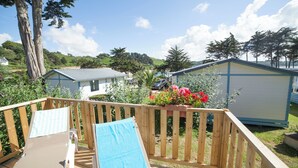 A wooden deck with a blue towel and a lounge chair, surrounded by a garden with red flowers and a shed.