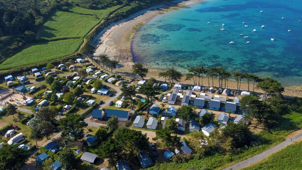 An aerial view of a coastal camping area with RVs and mobile homes, a beach, and clear blue waters with boats.