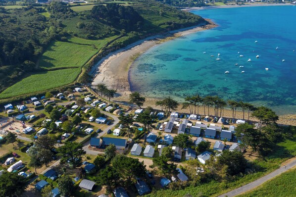 An aerial view of a coastal camping area with RVs and mobile homes, a beach, and clear blue waters with boats.