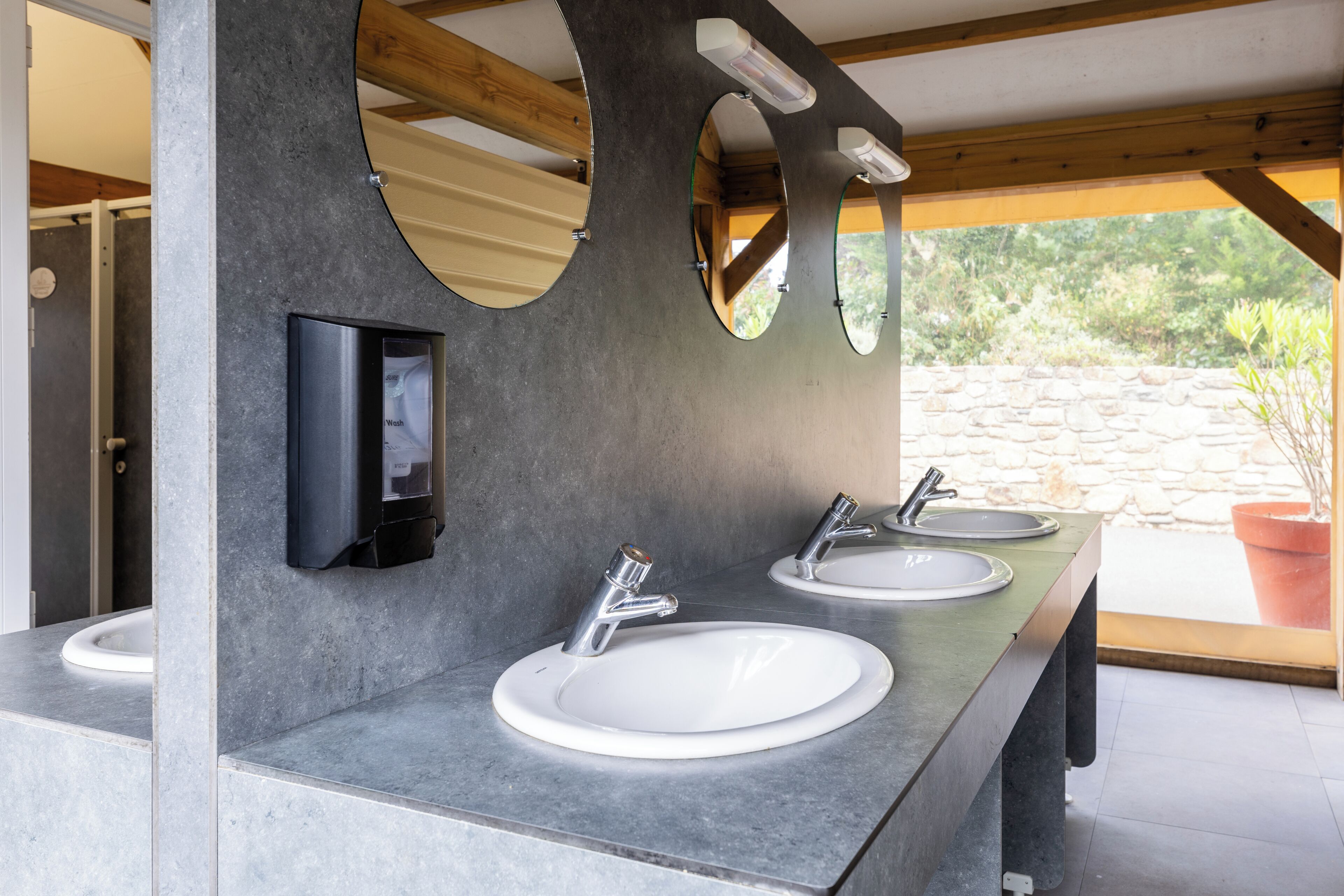 A modern bathroom with three sinks, a mirror, and a soap dispenser.