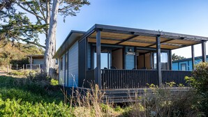 A modern cabin with a covered porch, a deck, and a view of the surrounding landscape.