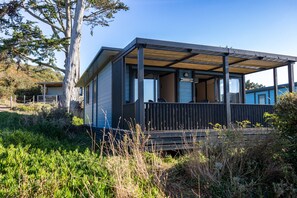 A modern cabin with a covered porch, a deck, and a view of the surrounding landscape.