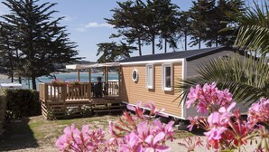 A wooden cabin with a deck, overlooking a body of water. - Camping RCN Port l'Épine (Trelevern)