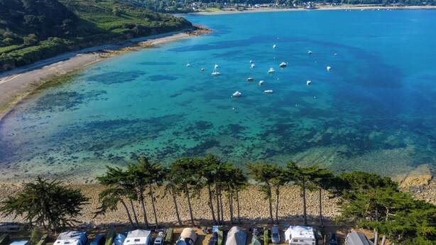 An aerial view of a coastal camping area with RVs and tents, clear turquoise waters, and boats. - Camping RCN Port l'Épine (Trelevern)