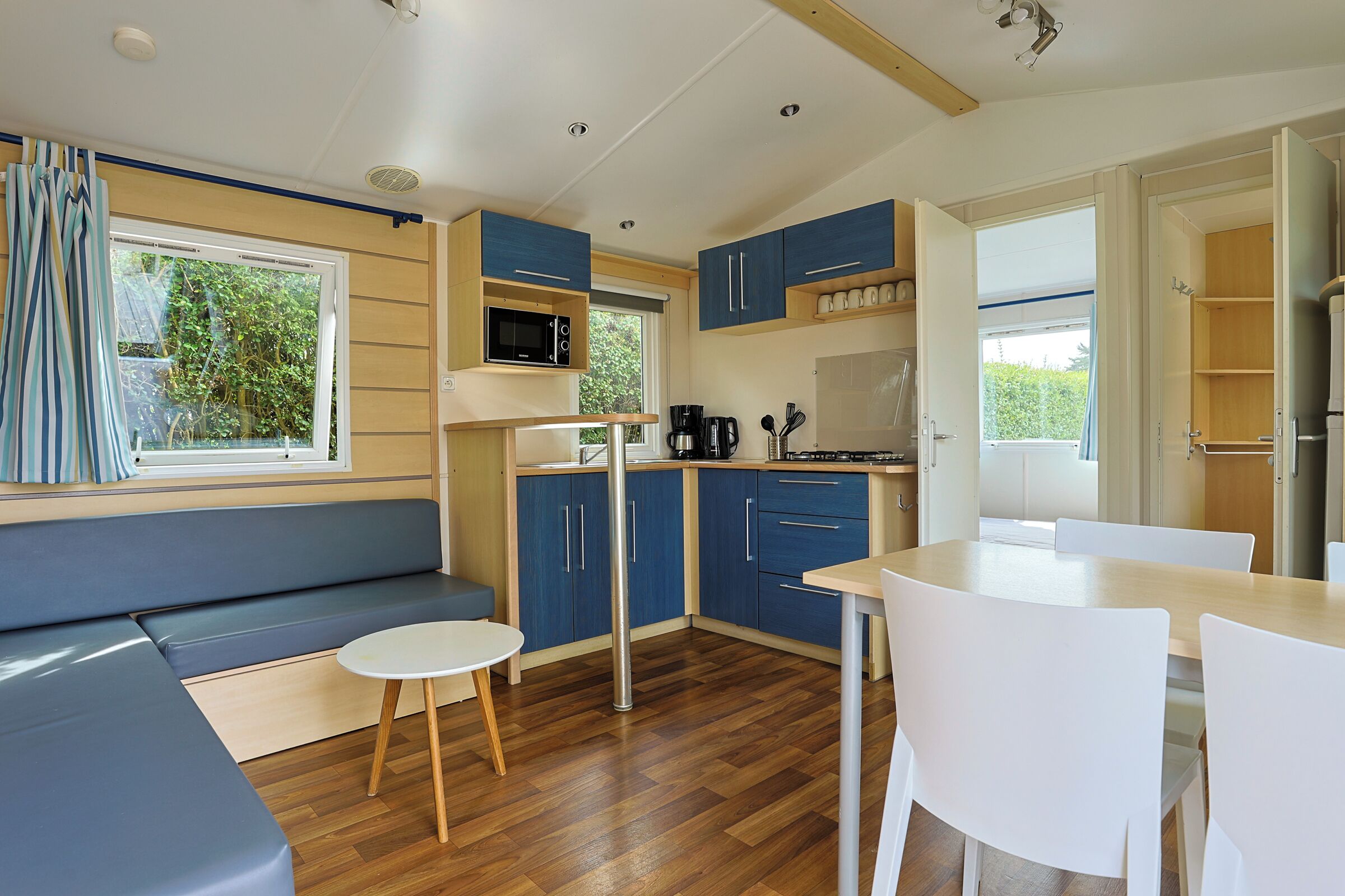 Cocina compacta con microondas, cafetera y pileta. Hay una zona de estar con un banco y una mesita redonda.