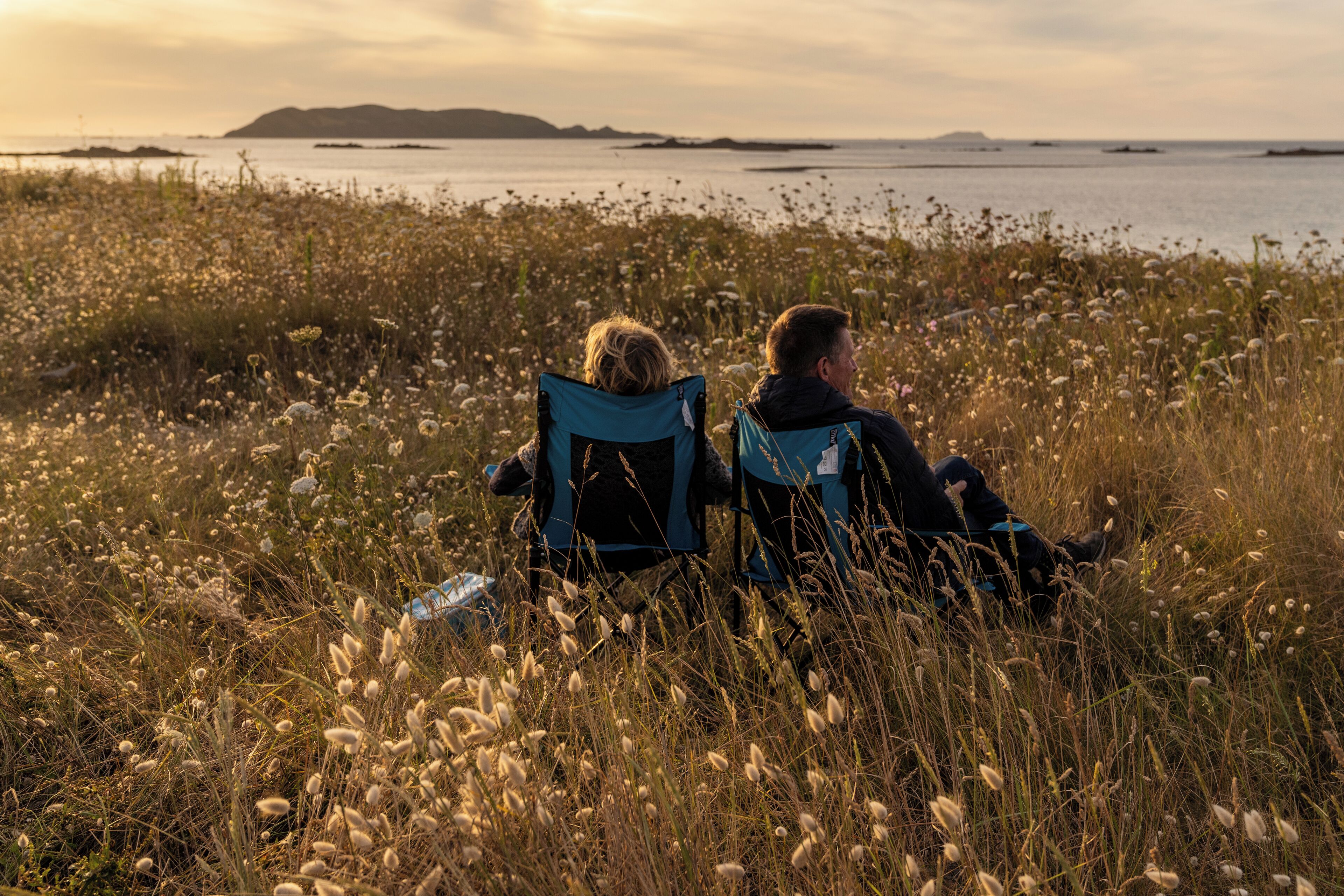 Two people sitting on chairs facing a body of water with a distant landmass.