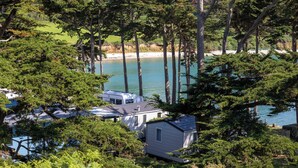A lakeside cabin with a small dock, surrounded by dense trees and a clear view of the lake. - Camping RCN Port l'Épine (Trelevern)