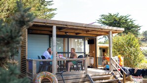 A wooden deck with a covered seating area, a small pool with a donut float, and a slide leading to a covered area. - Camping RCN Port l'Épine (Trelevern)