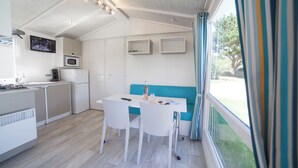 A modern kitchen with white cabinetry, a microwave, and a dining area with a table and chairs. - Camping RCN Port l'Épine (Trelevern)