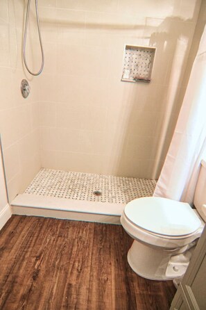 Ein Badezimmer mit Dusche, Toilette und einem gemusterten Boden.
