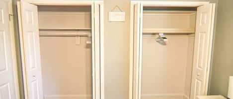 A room with two open closets, wooden flooring, and a small bedside table with a lamp.